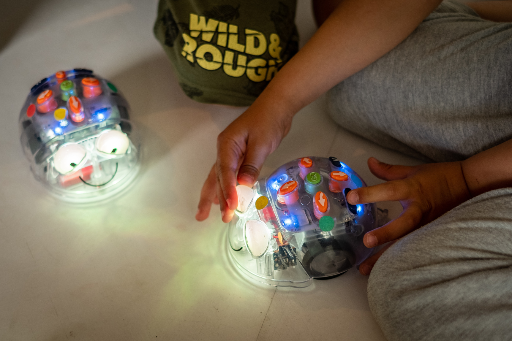 Ein Kind spielt mit zwei leuchtenden Robotern auf dem Boden
