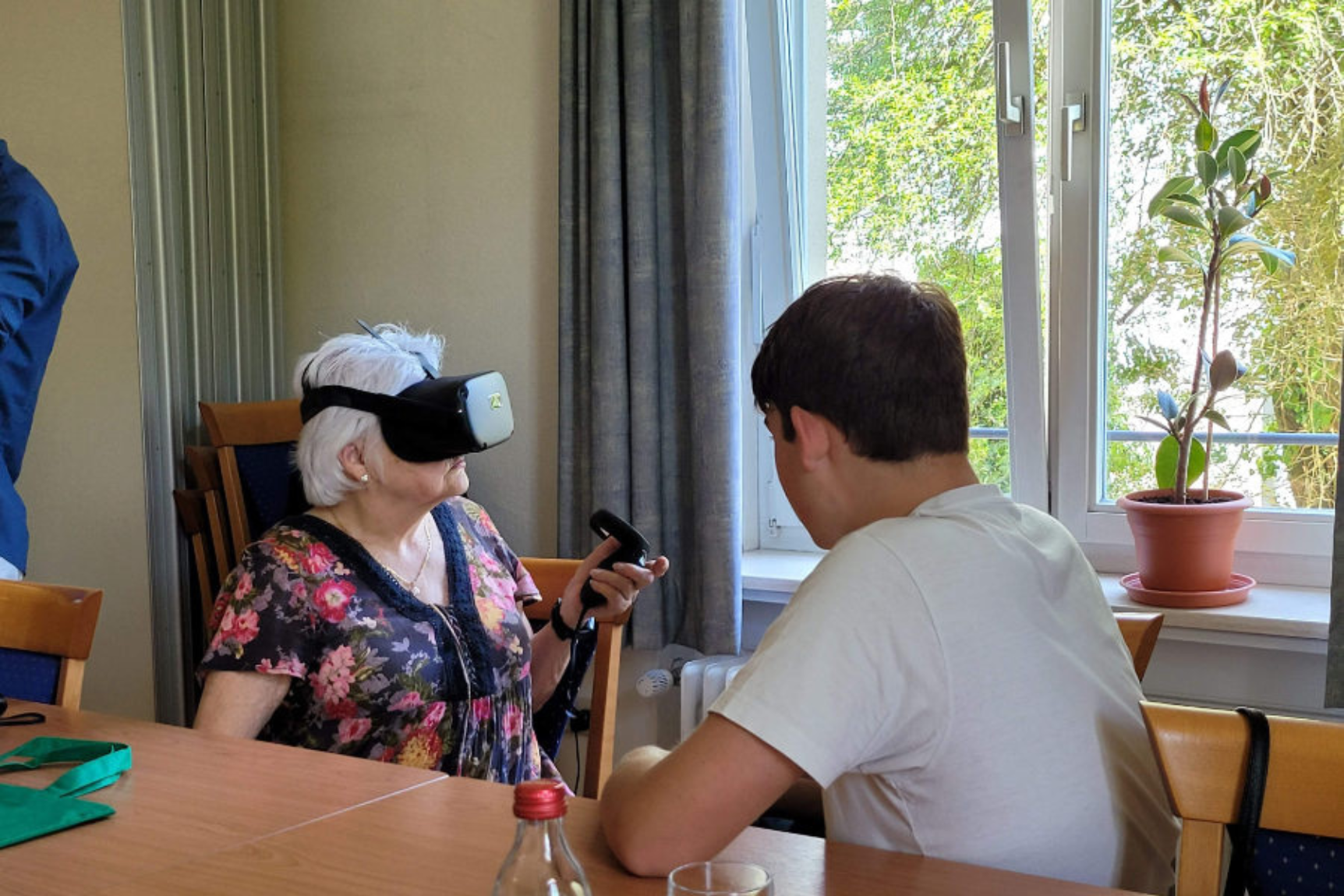 Ältere Frau erlebt Virtual Reality, ein jüngerer Mann sitzt ihr gegenüber