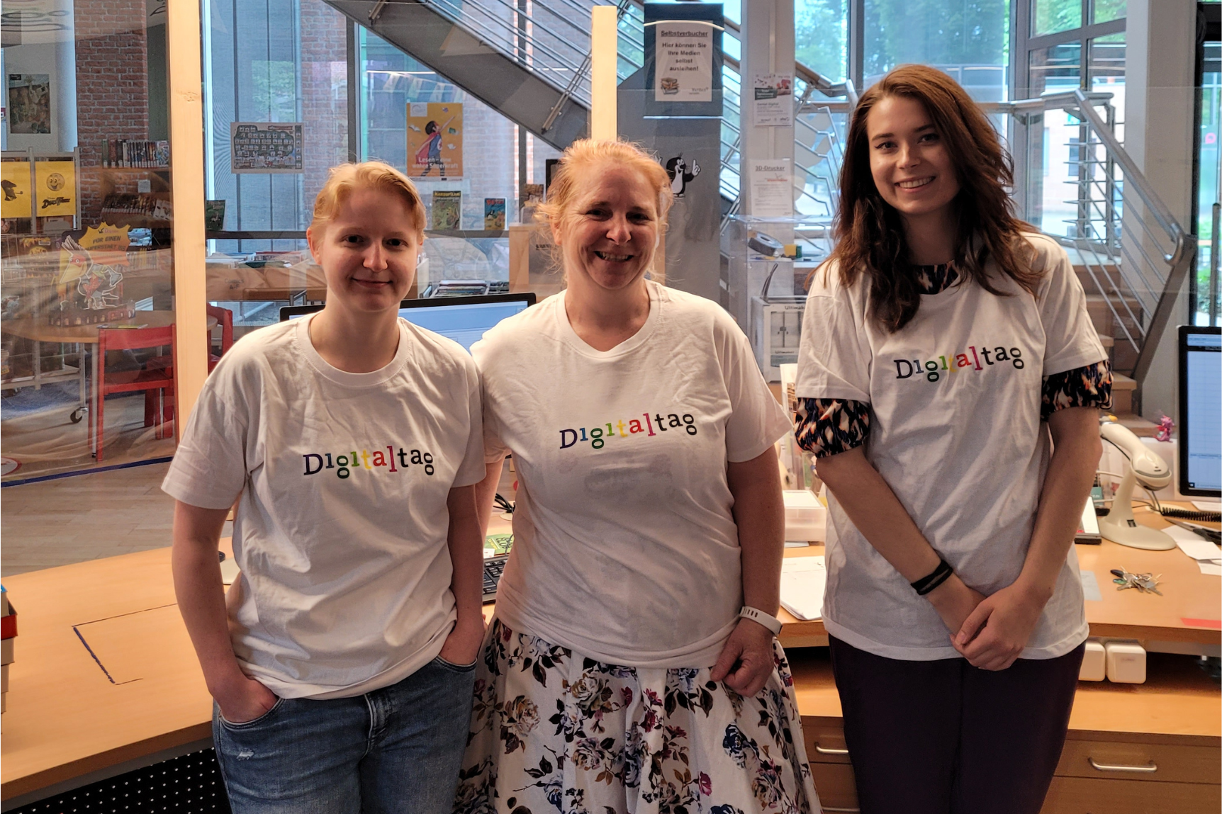 Drei Mitarbeiterinnen einer Bibliothek stragen Digitaltag-T-Shirts