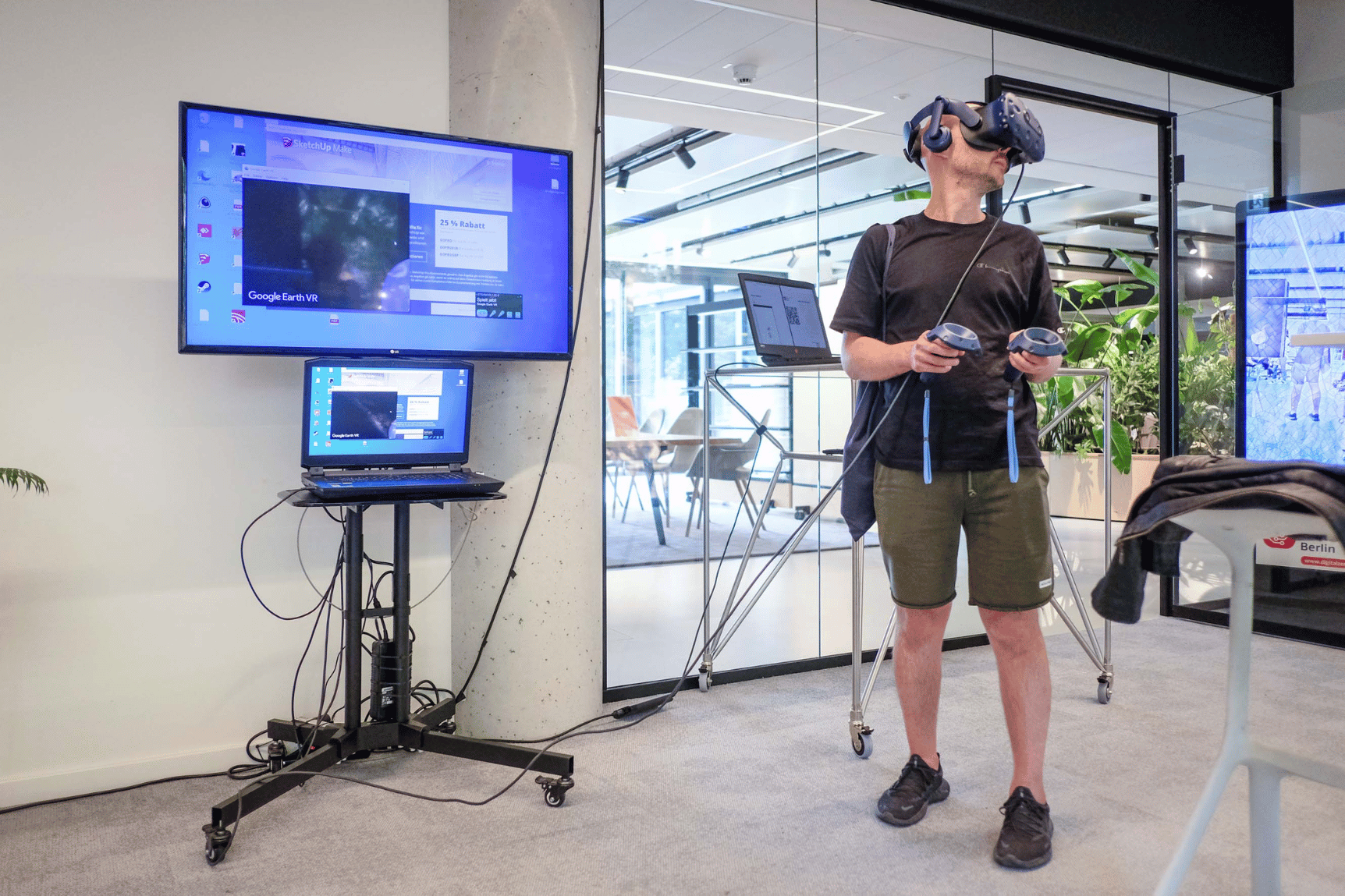 Ein Mann trägt einer VR-Brille und hält Controller in den Händen; die Geräte sind mit einem Laptop verkabelt