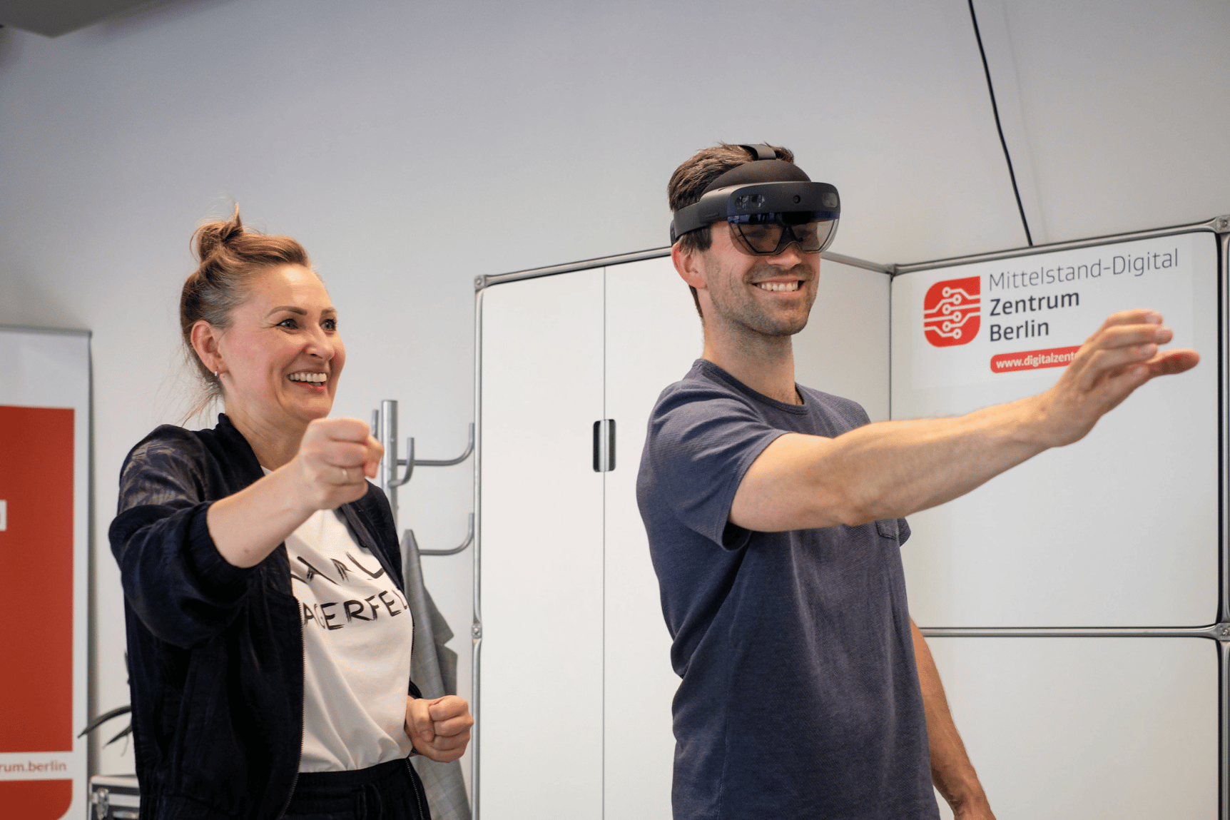 Ein Mann trägt einer VR-Brille und streck seinen rechten Arm aus, links neben ihm eine Frau ohne VR-Brille, die die gleiche Bewegung macht