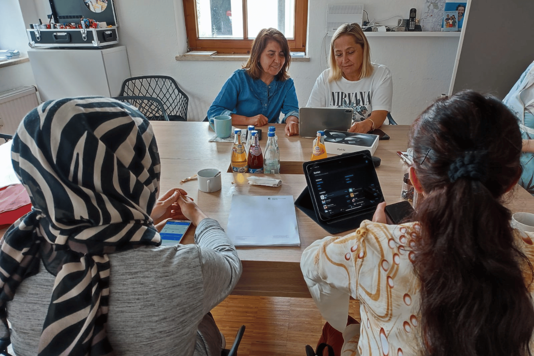 Eine Gruppe Frauen sitzt an einem Tisch und schaut sich zusammen die Bedienung eines Tablets an