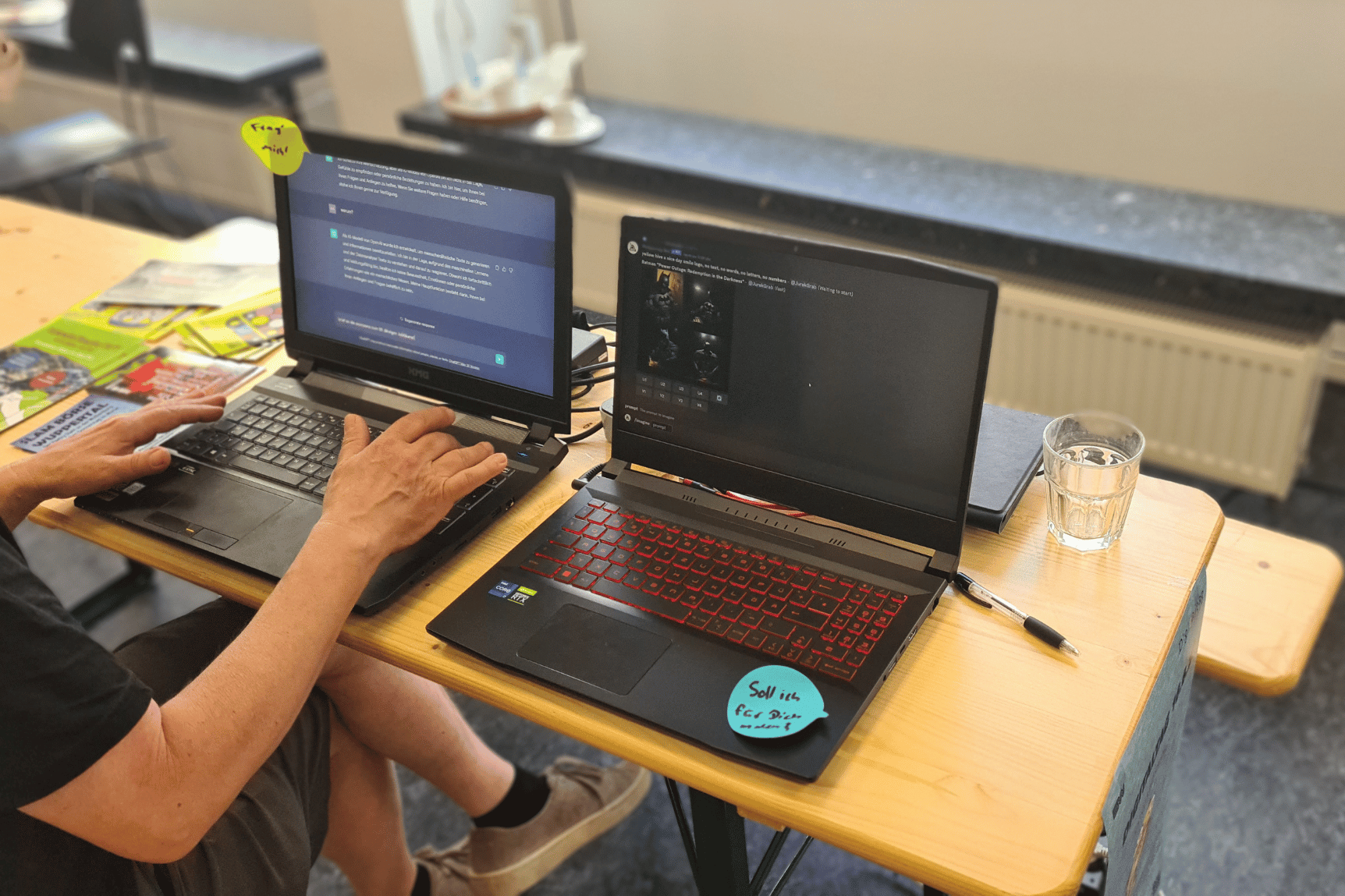 Zwei Laptops liegen geöffnet auf einem Schreibtisch, ein Mann sitzt an dem linken und tippt eine Frage für Chat GPT ein