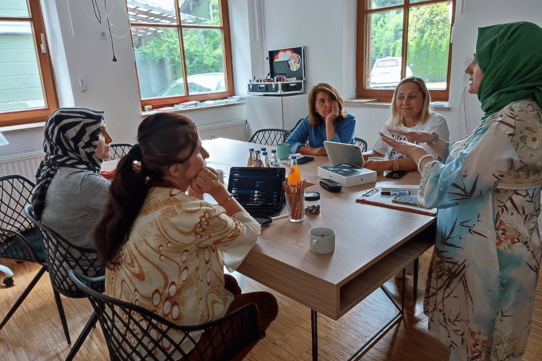 Eine Gruppe Frauen sitzt an einem Tisch, vorne steht eine Frau mit Kopftuch und erklärt ihnen etwas zur Nutzung digitaler Technologien