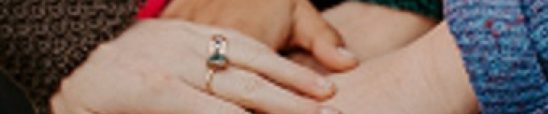 Viele Hände liegen Aufeinander als Zeichen des Zusammenhalts. Die Hand ganz oben trägt einen Ring am Ringfinger.