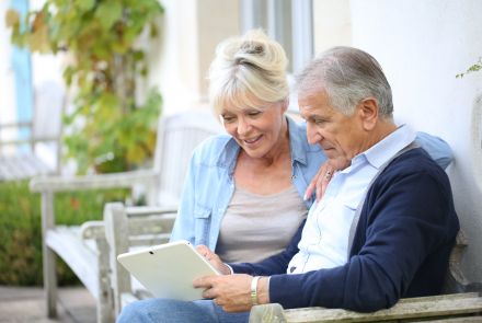 Zwei ältere Menschen sitzen im Freien vor einem Tablet.