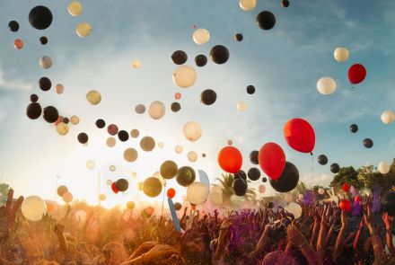 Luftballons steigen in den Himmel; eine Menschenmenge streckt die Arme in die Luft