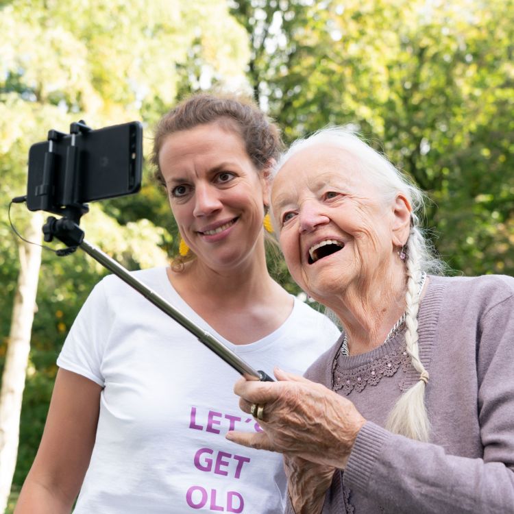 Eine ältere Dame schießt mit einem Selfiestick ein Foto von sich und einer jüngeren Frau, vielleicht ihre Enkelin. 