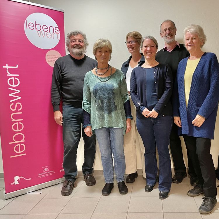 Gruppe von Menschen steht neben einem pinken Banner von "lebenswert"