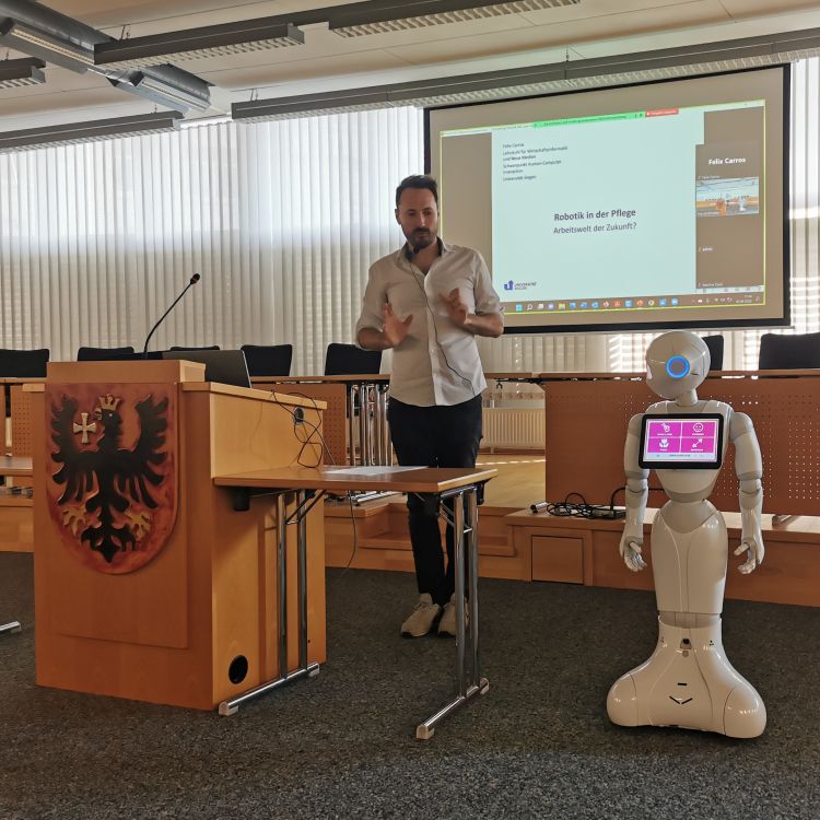 Ein Mann hält einen Vortrag zum Thema humanoide Roboter, neben ihm steht ein Roboter