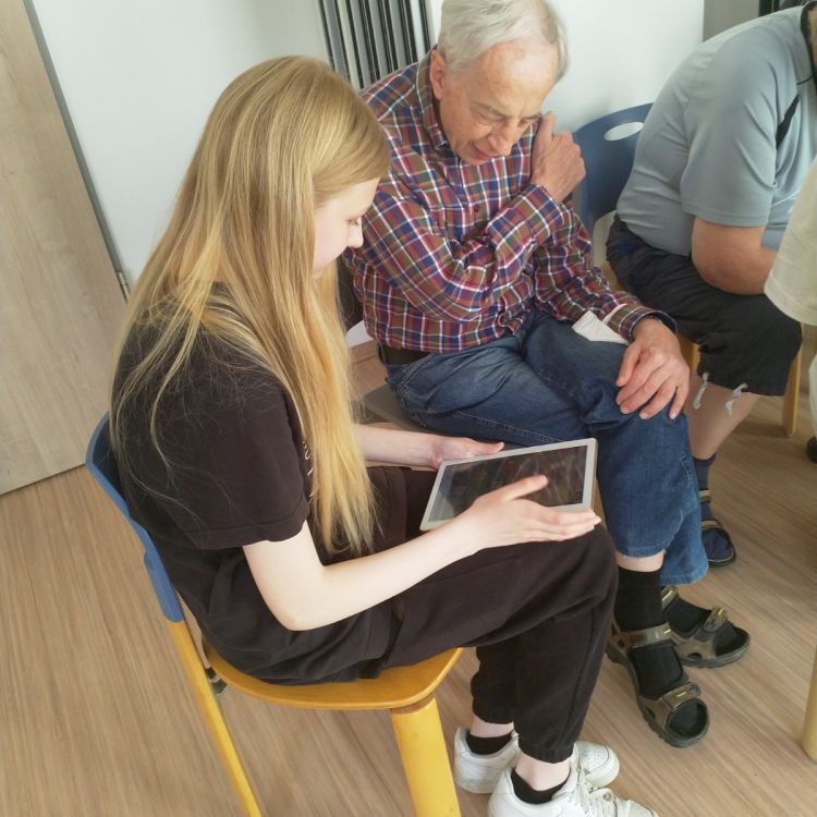 Eine junge Frau zeigt einem älteren Herren, wie man ein Tablet benutzt.