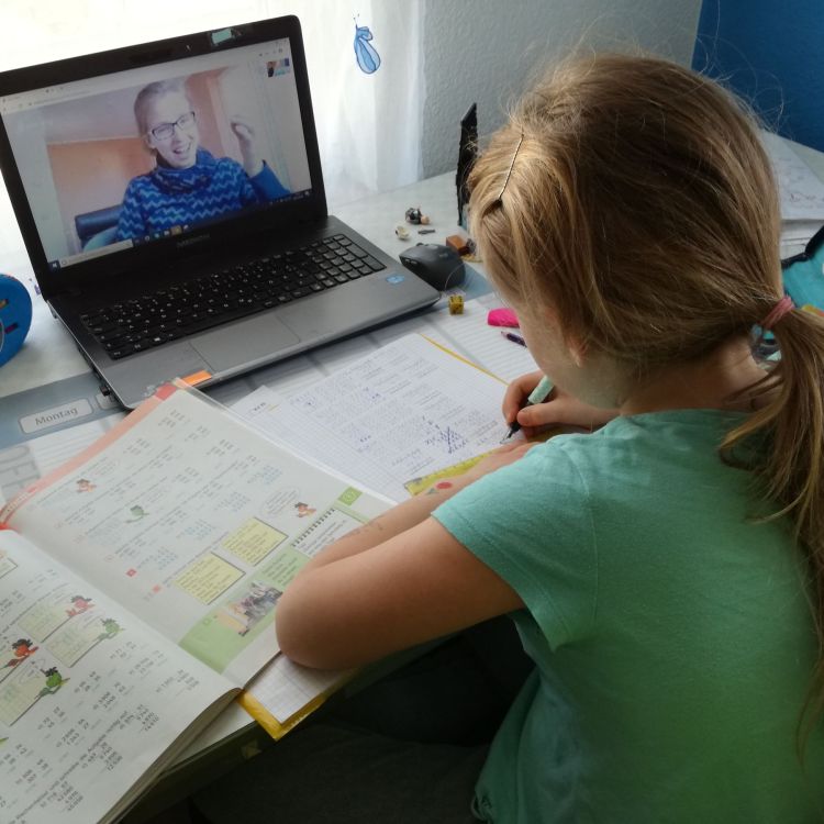 Mädchen von hinten an Schreibtisch vor Laptop in Videotelefonat