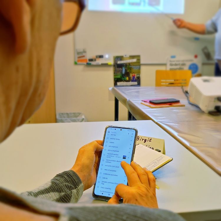 Person mit Handy in der Hand an einem Schreibtisch