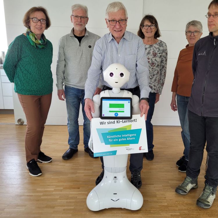 Ein Roboter einem Schild "KI-Lernort" steht vor einer Gruppe Menschen.