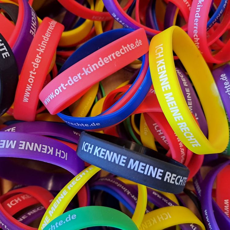 Viele bunte Gummiarmbänder liegen übereinander. Sie tragen die Aufschrift: Ich kenne meine Rechte.