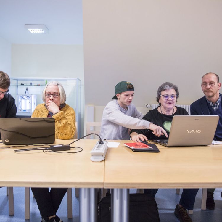  Eine Gruppe von Menschen sitzt um einen Tisch mit Laptops und diskutiert angeregt.