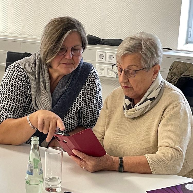 Eine Frau berät eine ältere Frau bei der Nutzung eines Smartphones