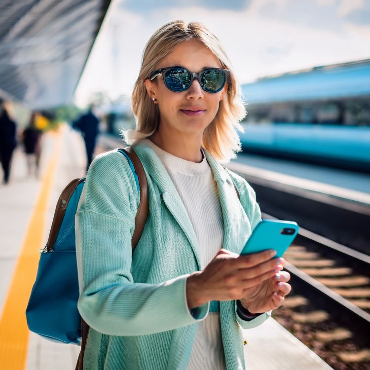 KI-generiertes Bild einer blinden Frau auf einem Bahnsteig mit einem türkisen Handy in der Hand