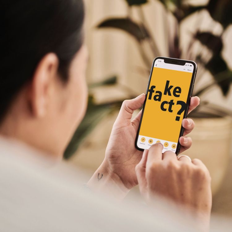 Eine Person am Smartphone, auf dem Bildschirm ist zu sehen "fake / fact?"