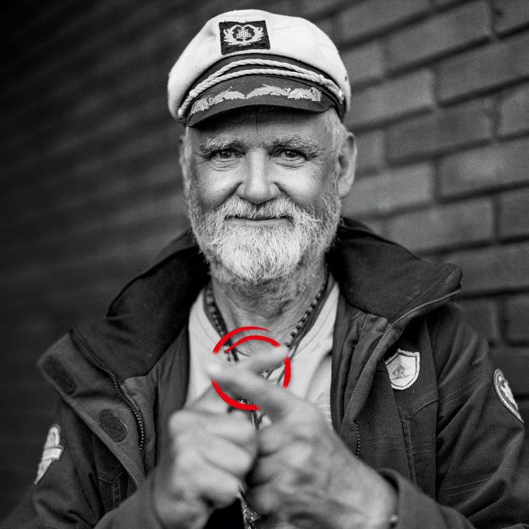 Schwarz-weiß-Foto eines älteren Mannes, der mit seine Zeigefinger überkreuzt hält. Das Kreuz ist rot eingekringelt.