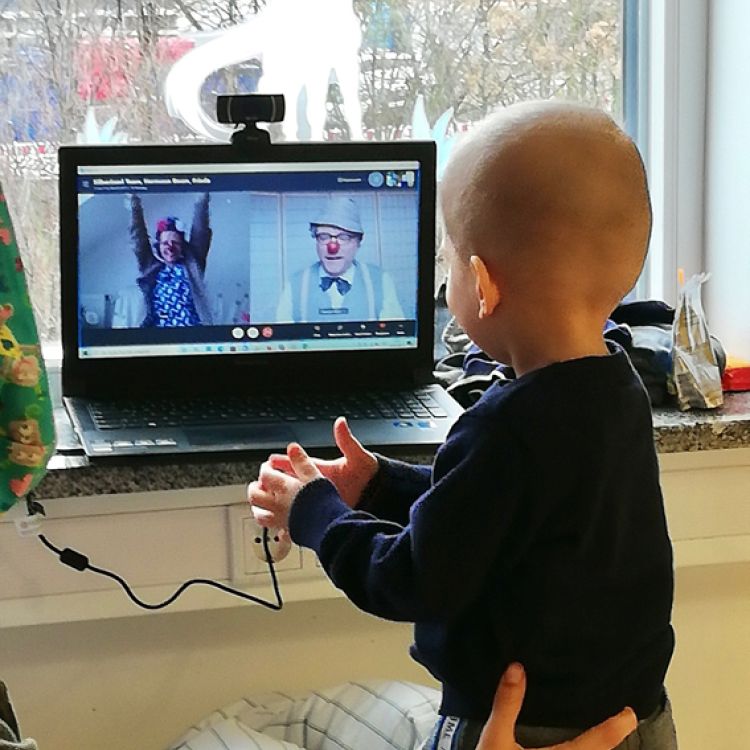 Ein Kind interagiert mit zwei Klinikclowns, die remote über einen Laptop zugeschaltet sind.